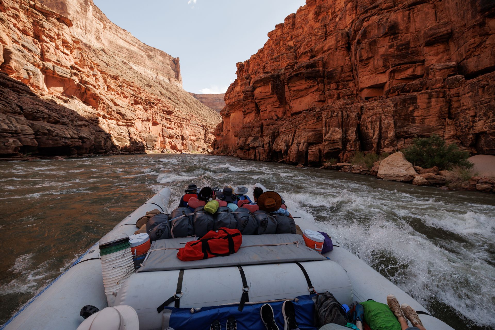 Rafting through a canyon; people on a boat, red rock walls on either side, and a rushing river.
