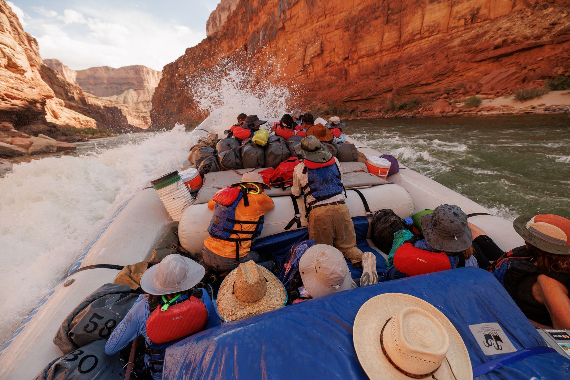 Rafting on whitewater river in a canyon. People in life jackets navigate through a wave, splashes everywhere.