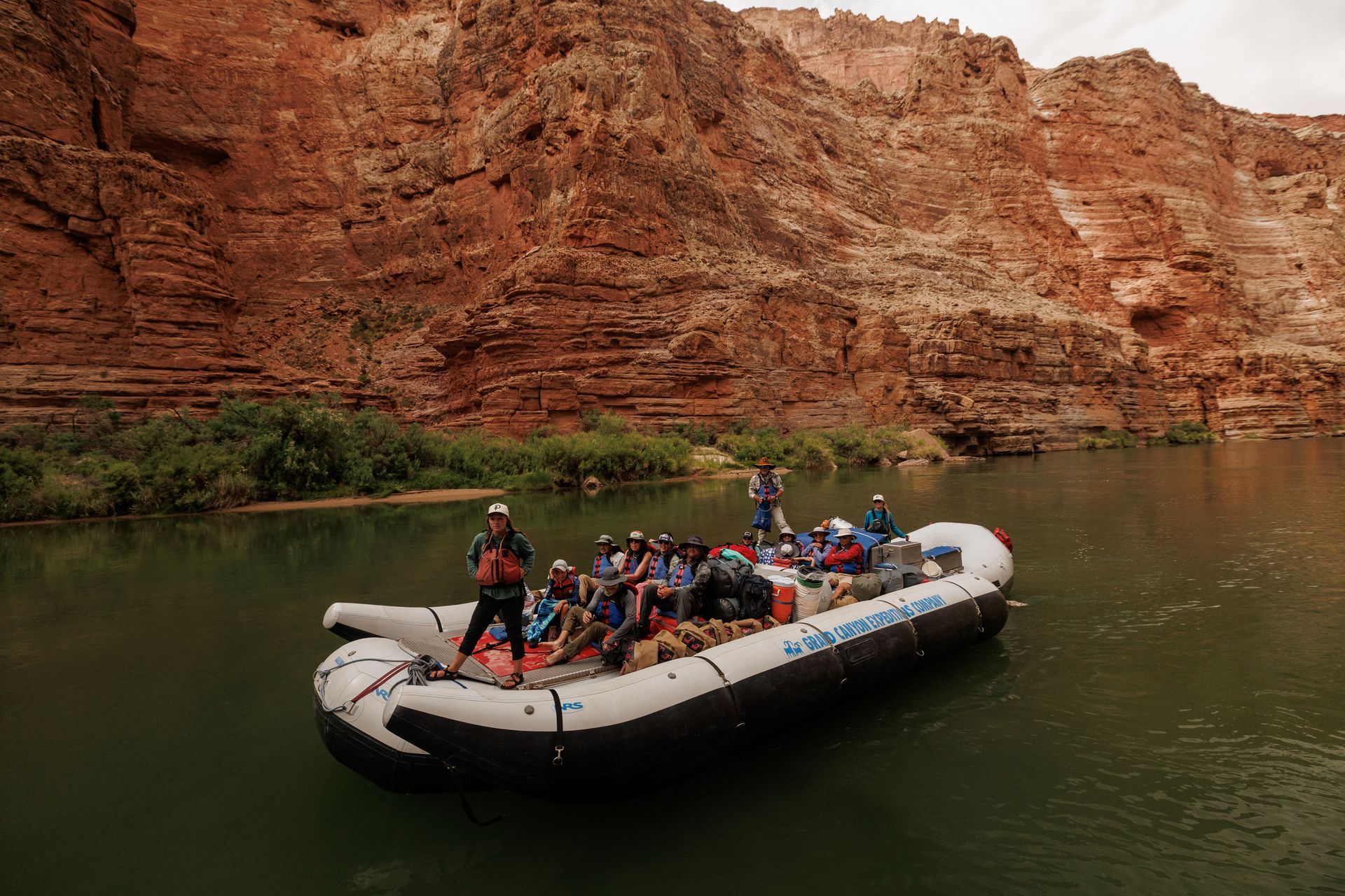 Raft on a river with people, red rock canyon in background.