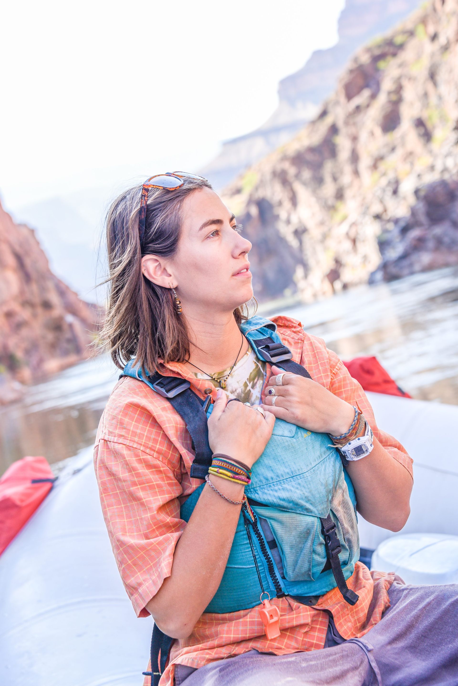 Woman on a raft in a canyon, wearing a life vest, looking up at the scenery.