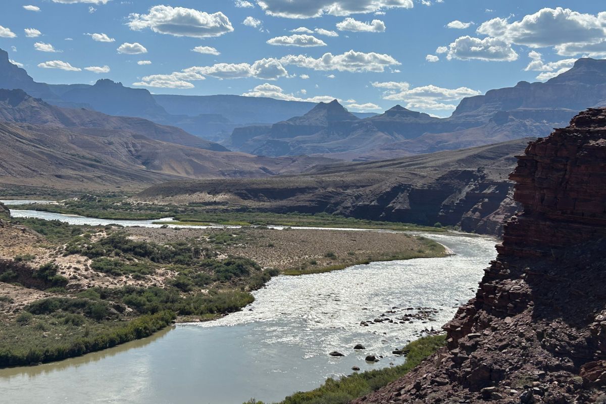 River winding through a canyon, with distant mountains under a blue sky with clouds.