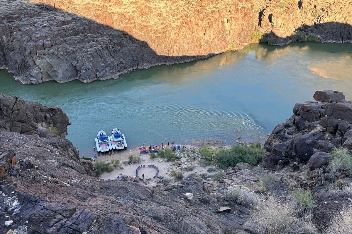 Overlooking a river with boats at a sandy beach below cliffs in daytime sun.