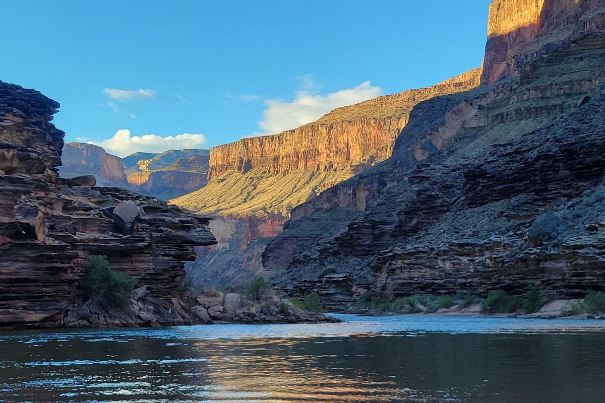 Canyon landscape with water reflecting the layered rock walls, under a blue sky.