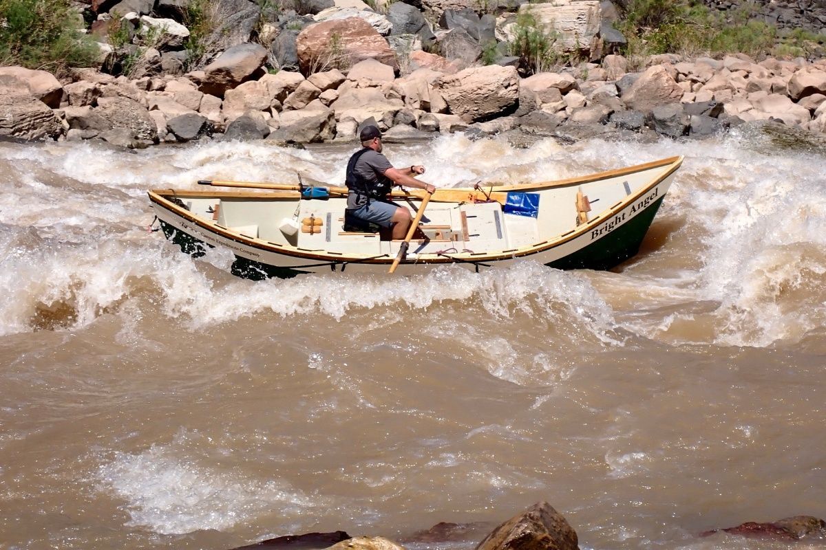 A man is rowing a boat in a river with a license plate that says e1