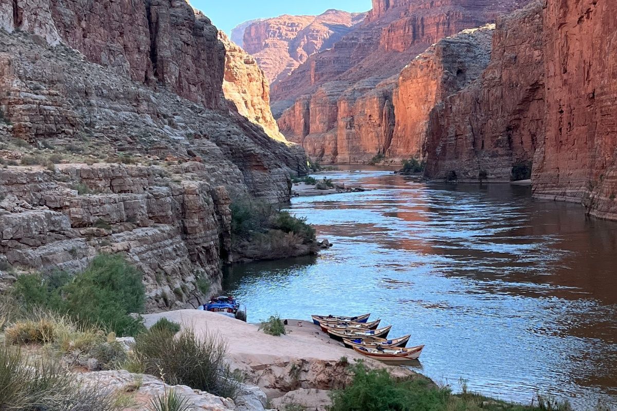 A row of boats are docked on the shore of a river in a canyon.