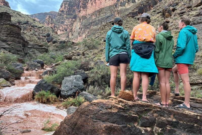 A group of people standing on a rock overlooking a river