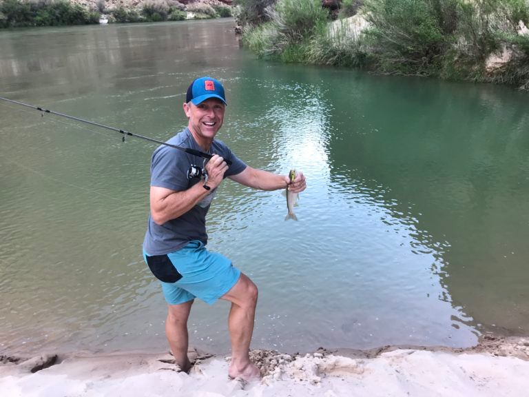 A man is standing next to a river holding a fishing rod and a fish.