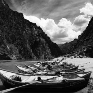 A row of boats are lined up on the shore of a river.