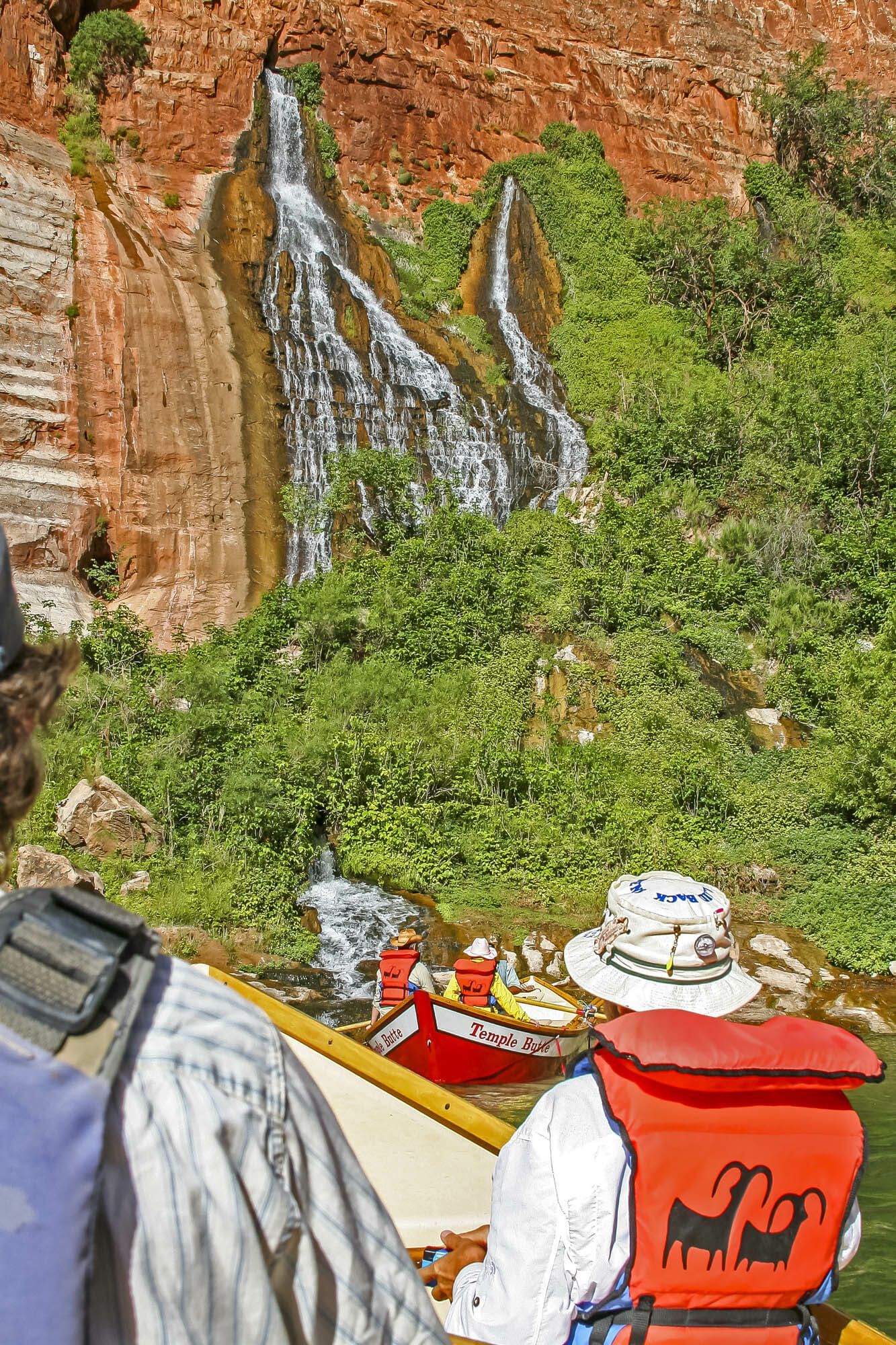 A man wearing a life jacket with a sheep on it looks at a waterfall