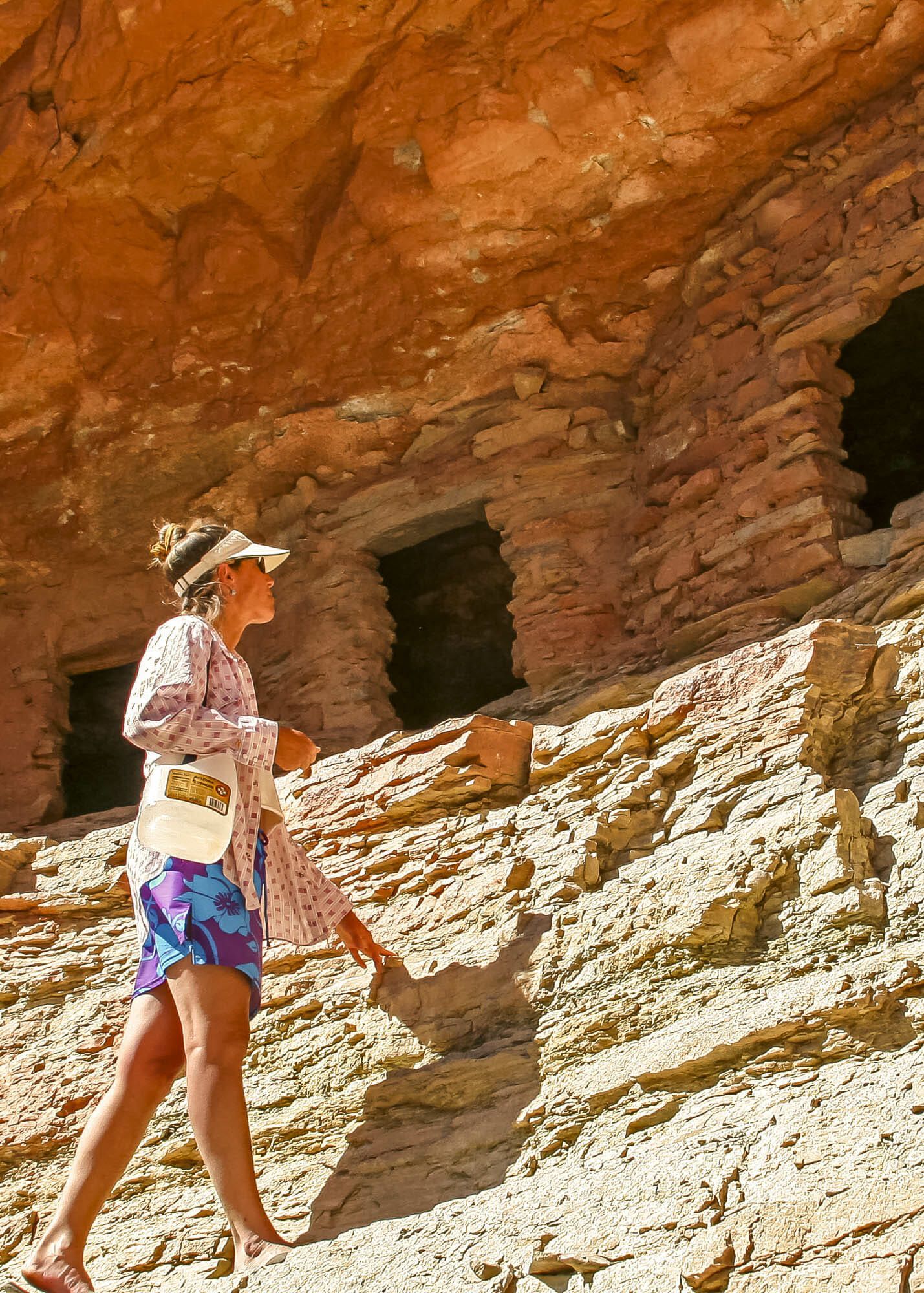 A woman wearing a visor and shorts is walking through a rocky area