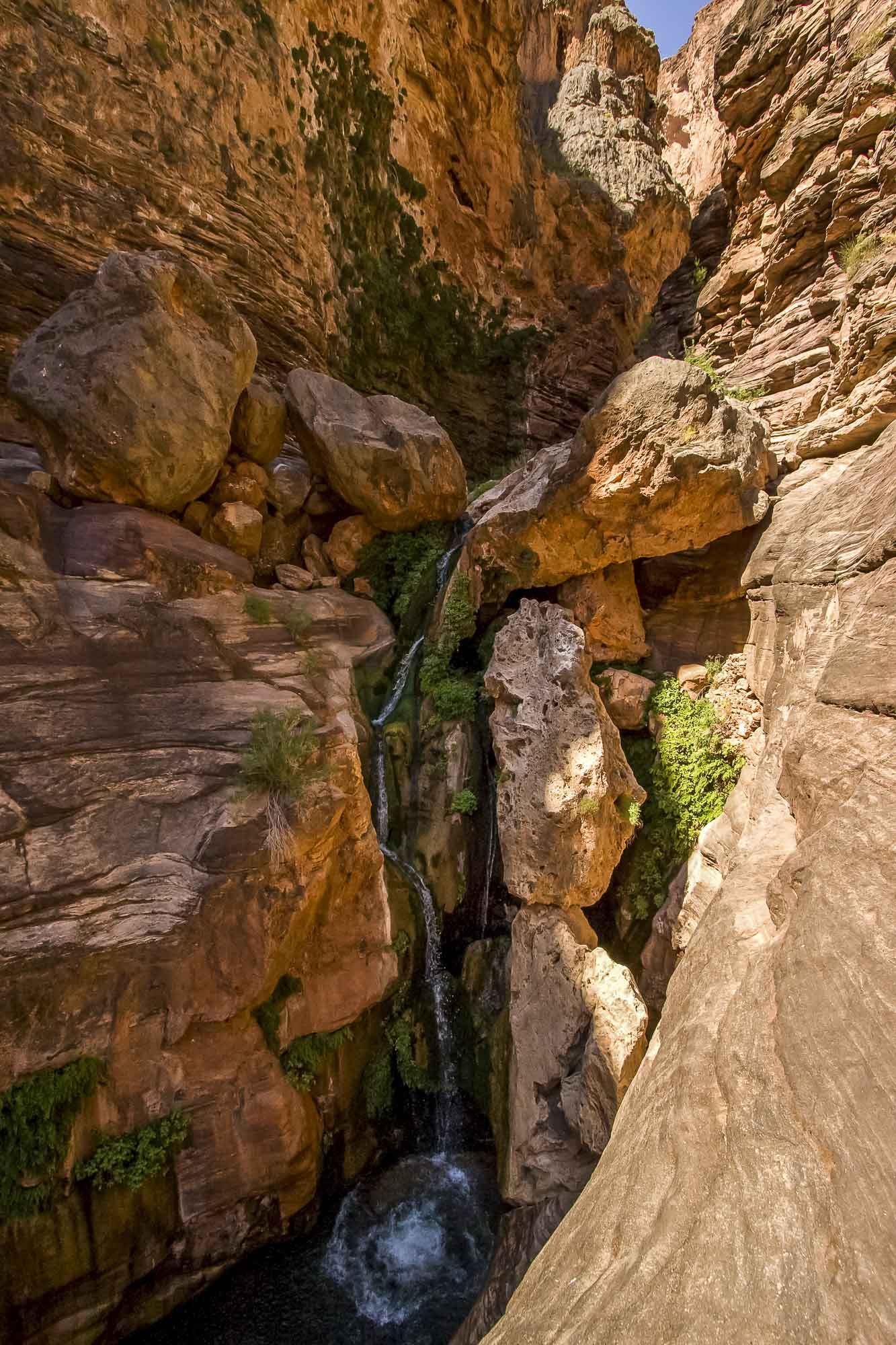 A small waterfall in the middle of a canyon surrounded by rocks.