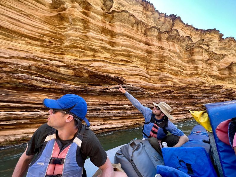 A man in a blue hat is pointing at something in the water