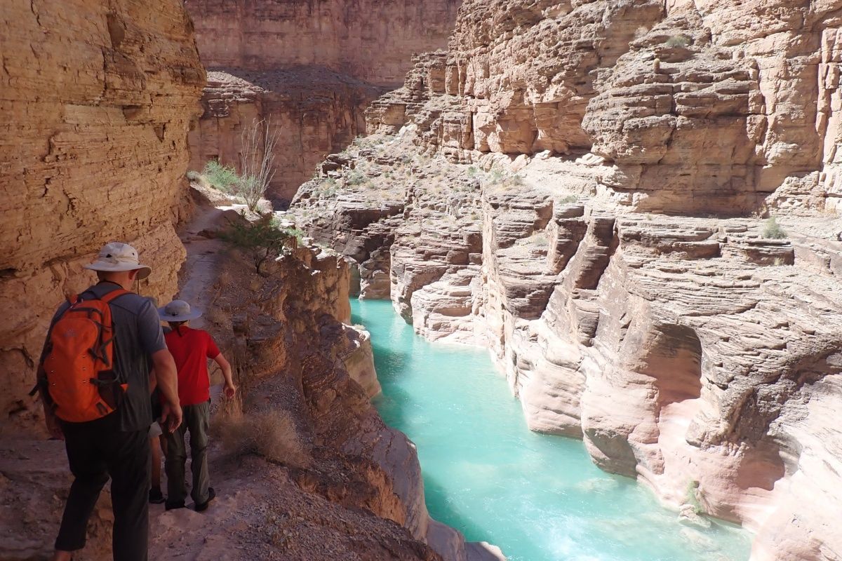 A couple of people standing next to a river in a canyon.