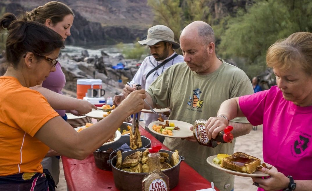 A group of people are standing around a table eating food.