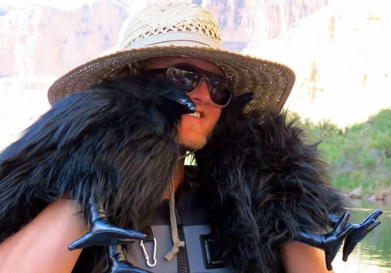 A man wearing a straw hat and sunglasses has a black fur coat around his neck
