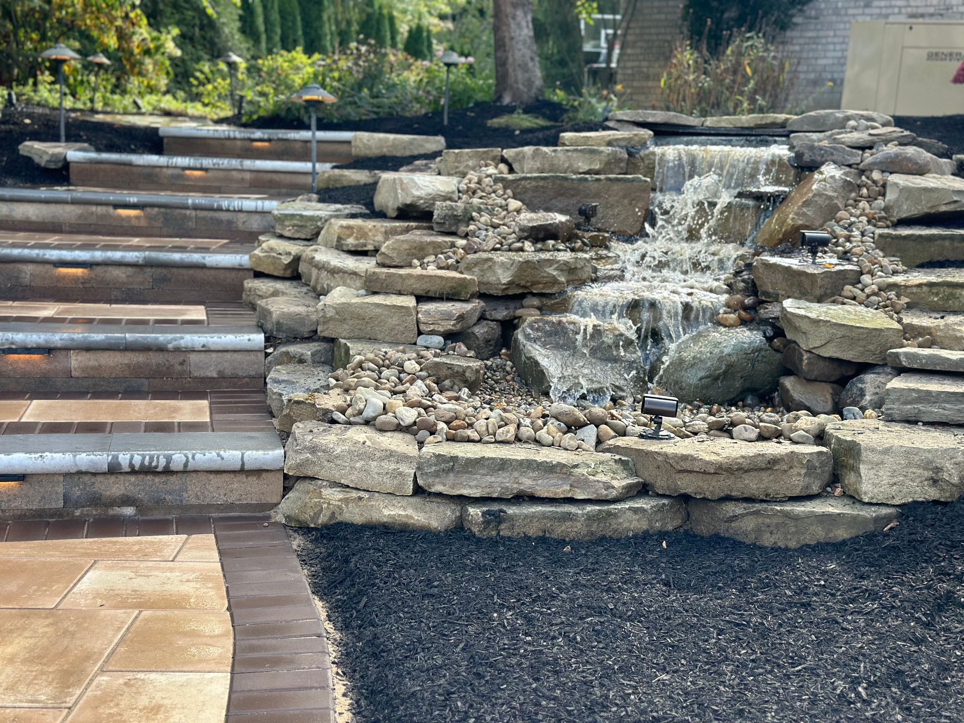 A waterfall is surrounded by rocks and stairs in a garden.