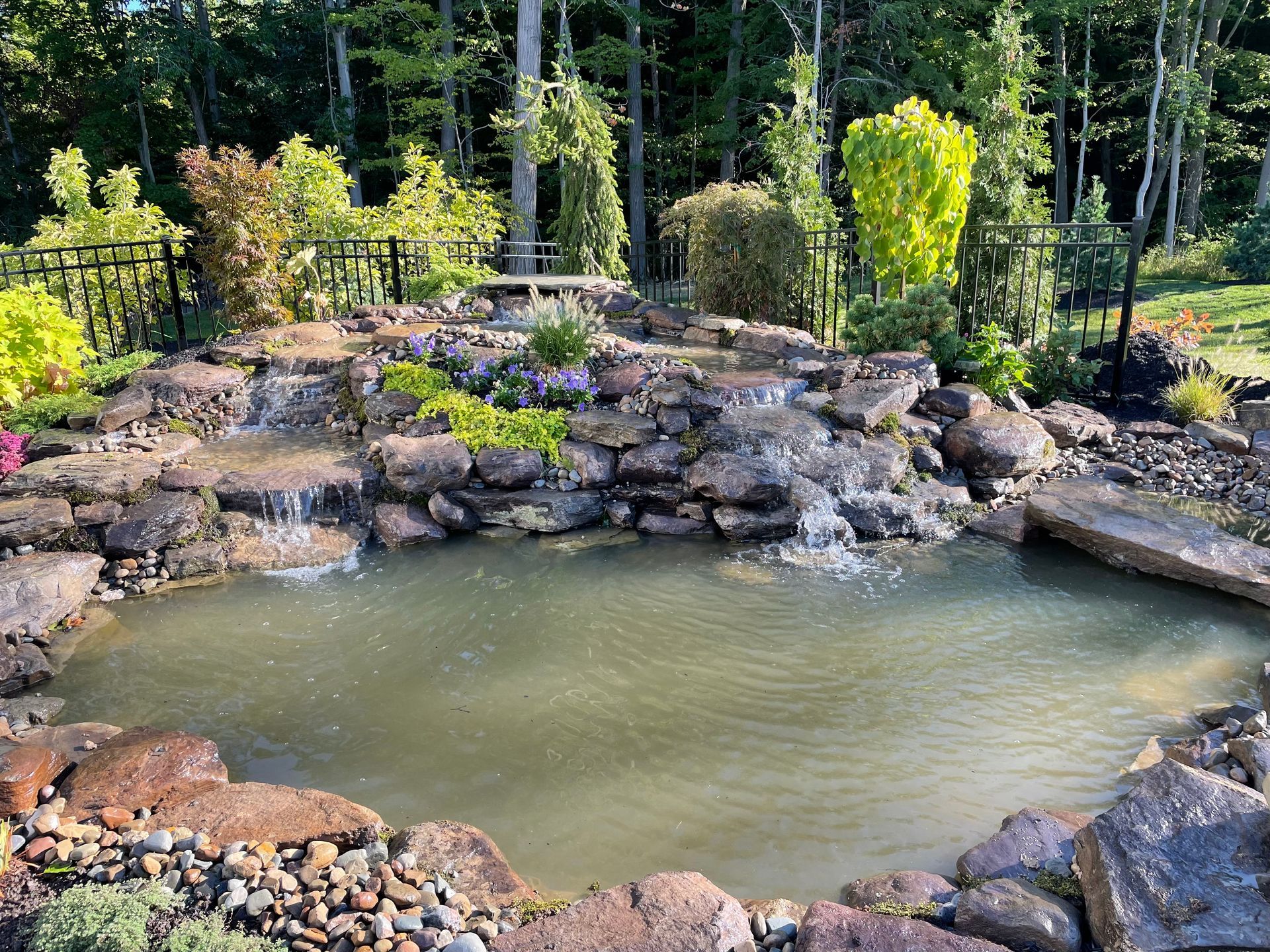 A large pond surrounded by rocks and trees with a waterfall in the middle.