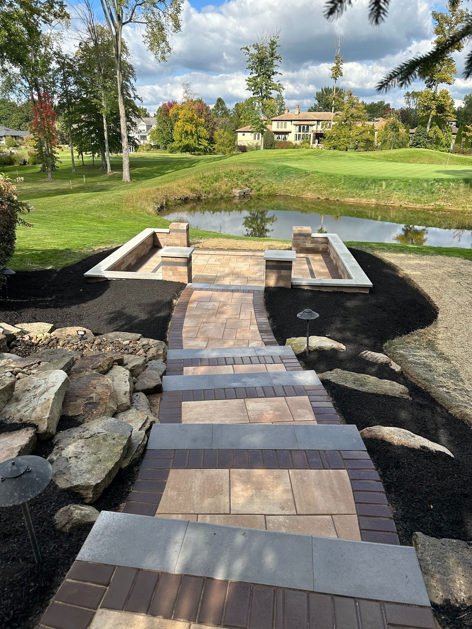 A brick walkway leading to a pond in a park.