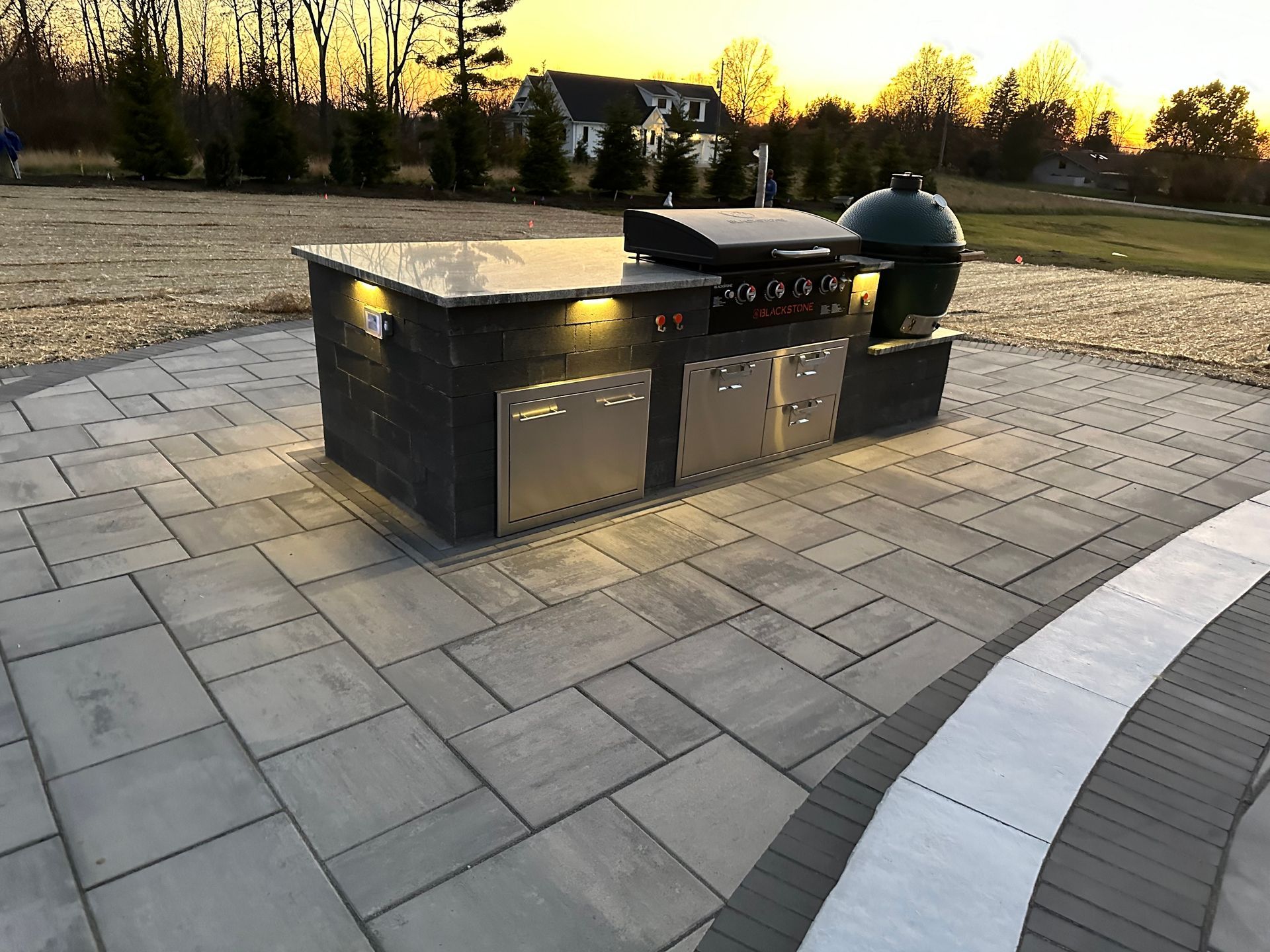 A large grill is sitting on a patio with a sunset in the background.
