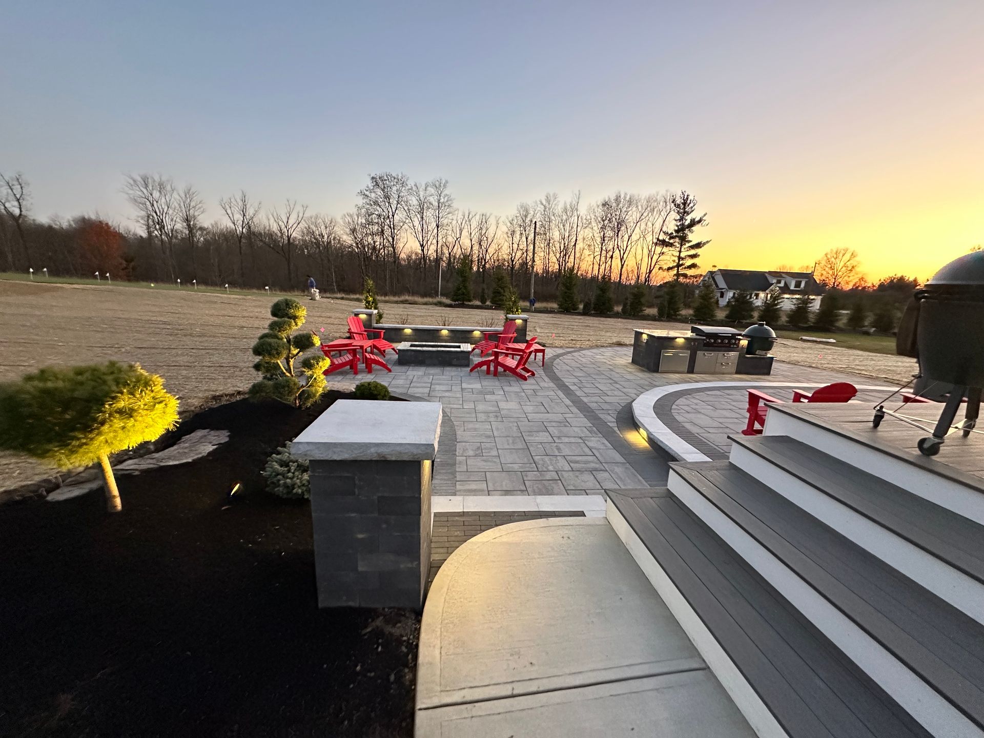 A patio with red chairs and a grill at sunset.