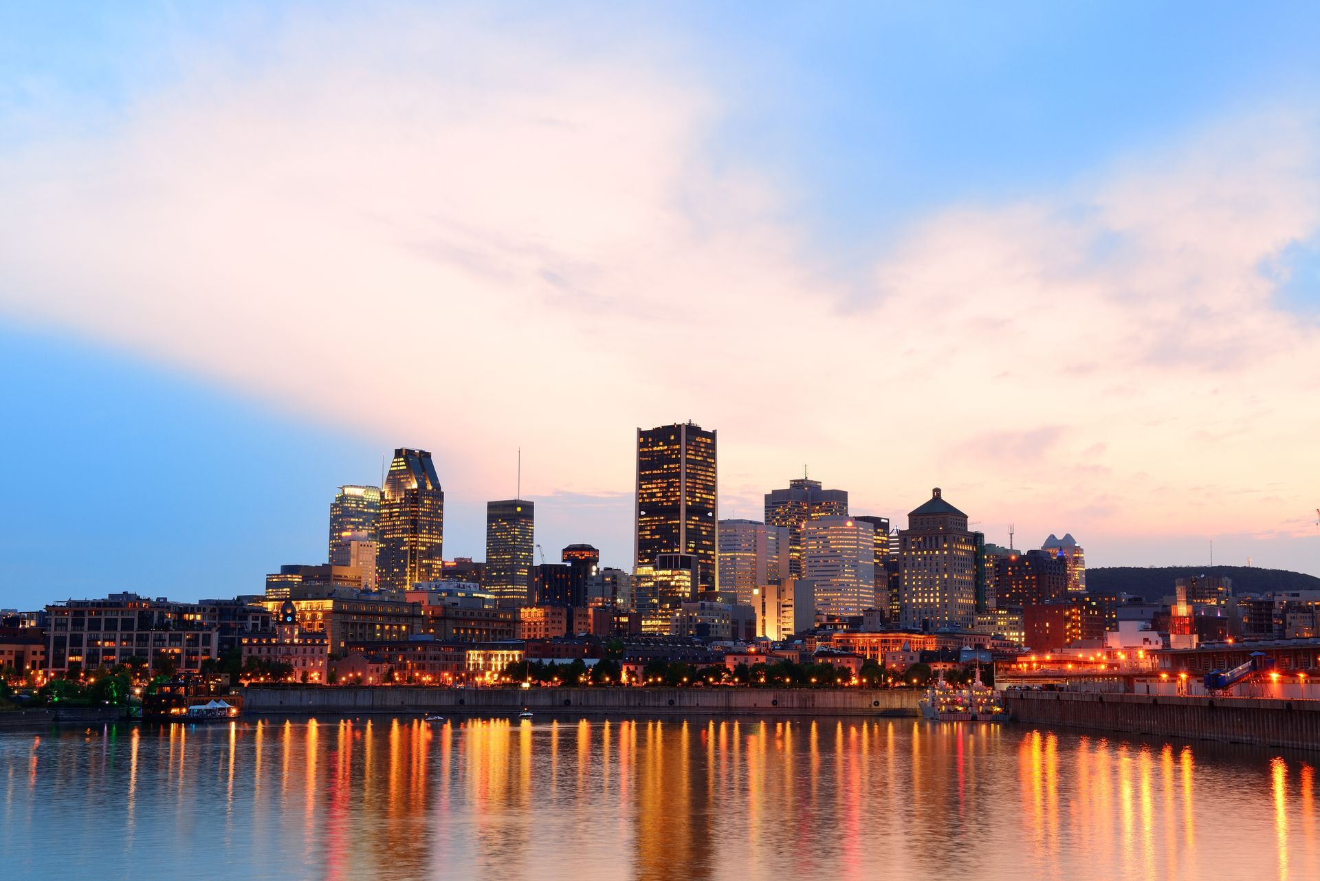 Montreal skyline at dusk, with lights reflecting in the water under a colorful sky.