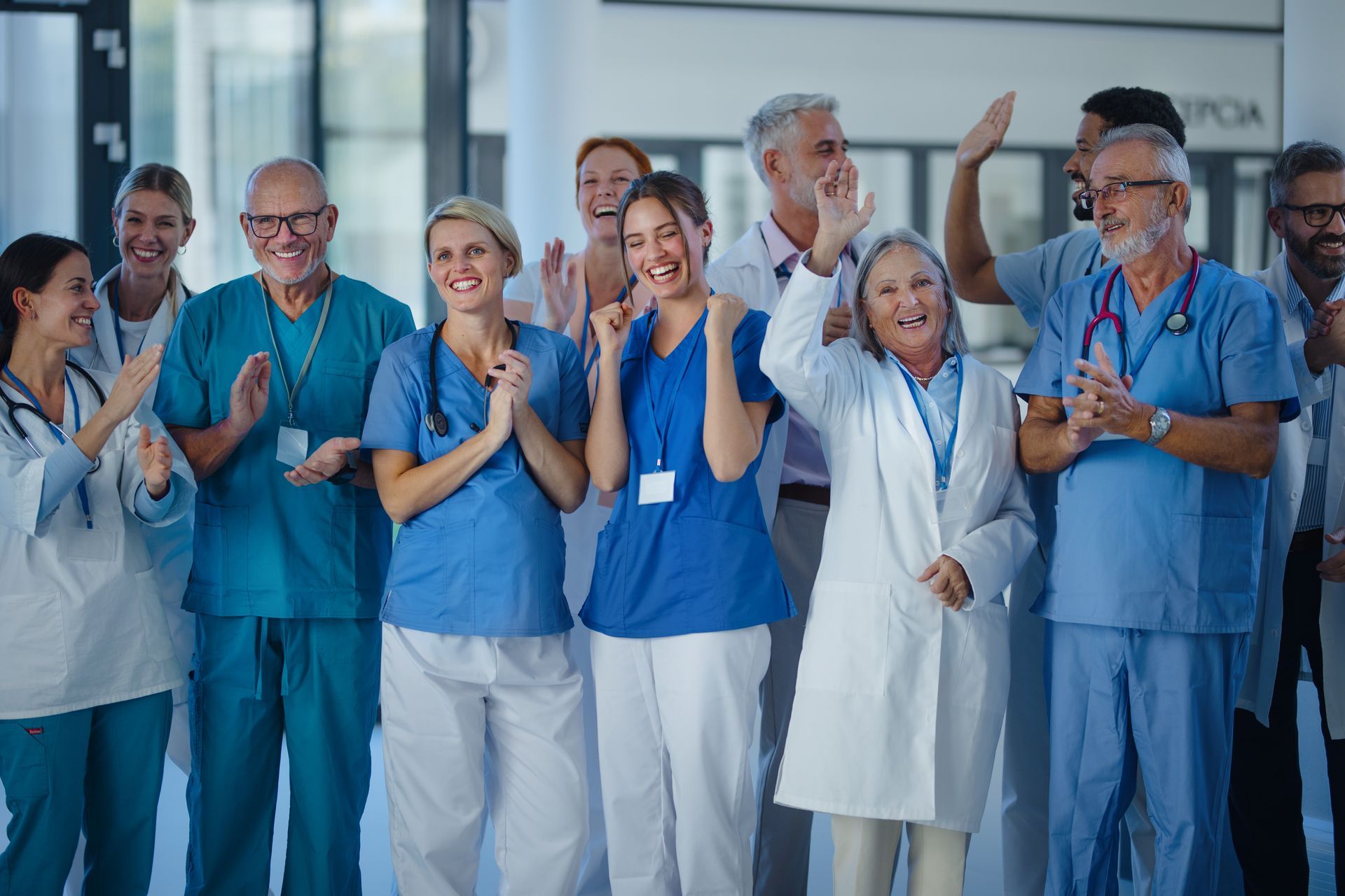 Medical staff in scrubs and white coats cheering and clapping in a hospital hallway, celebrating a success.