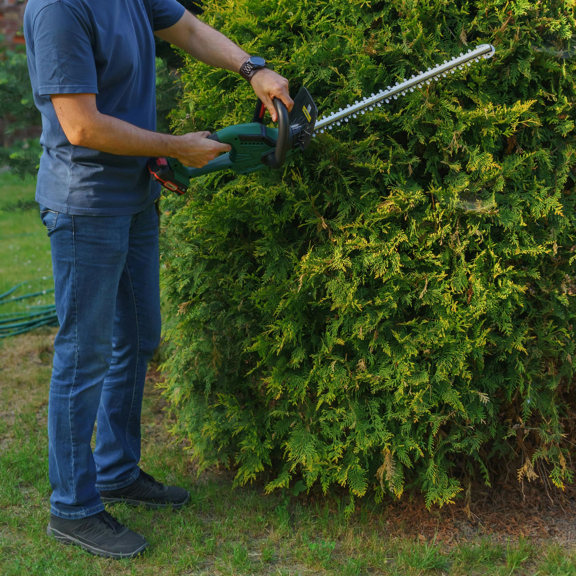 Person using an orange and black chainsaw to cut a tree trunk outdoors.