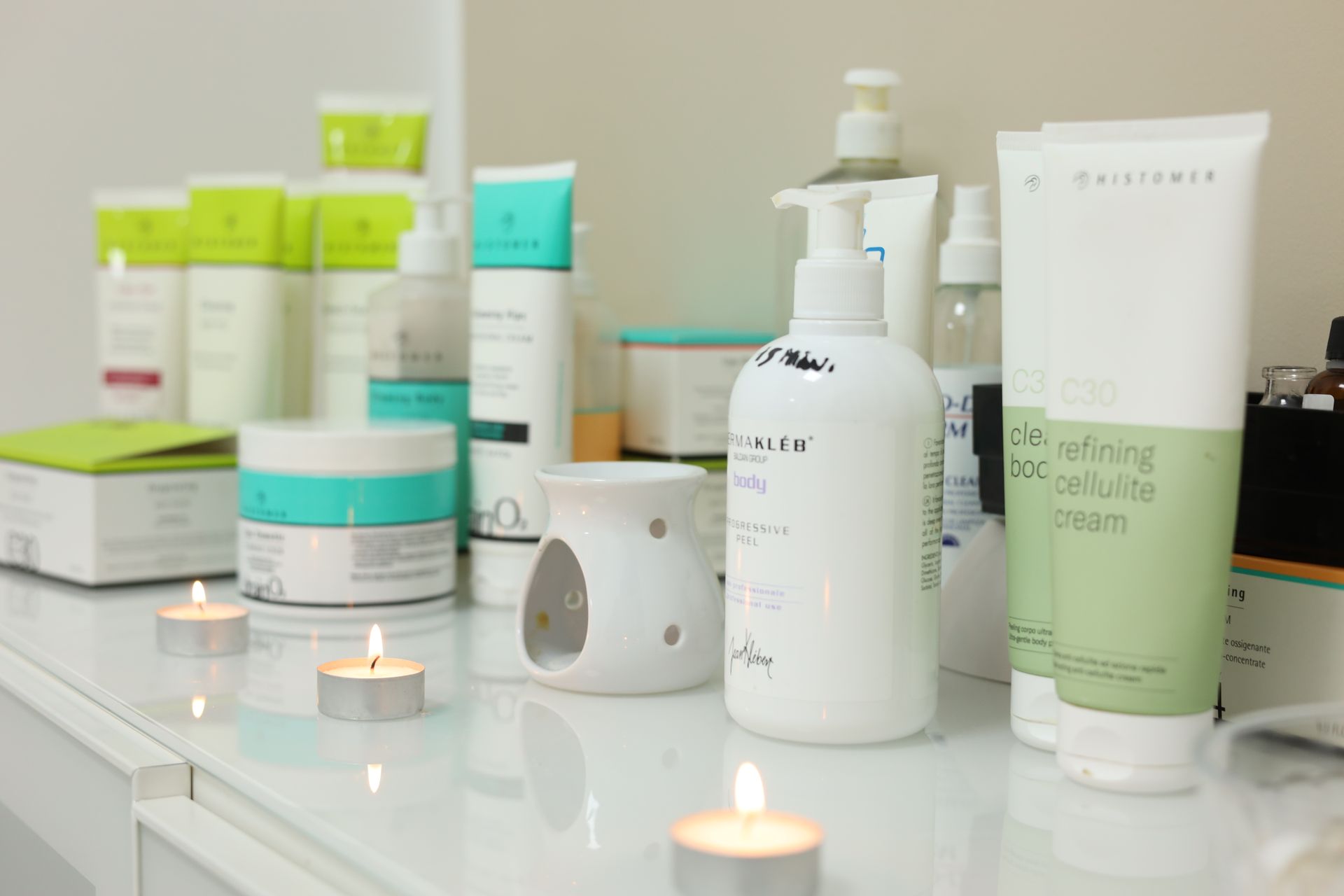 Prodotti di bellezza bianchi su uno scaffale, illuminati da piccole candele, in un ambiente da spa.