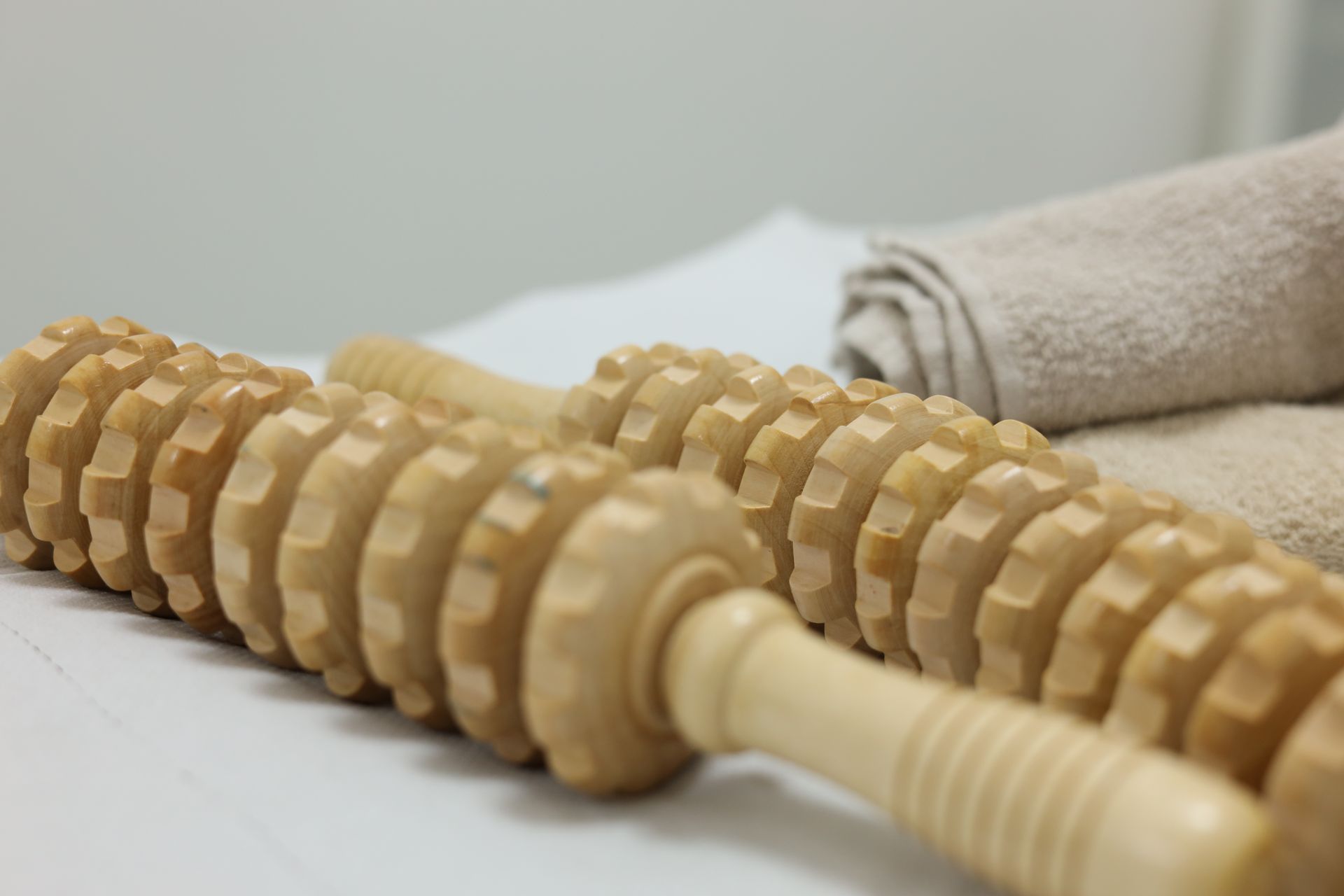 Due rulli massaggianti in legno su una superficie bianca con asciugamani arrotolati.