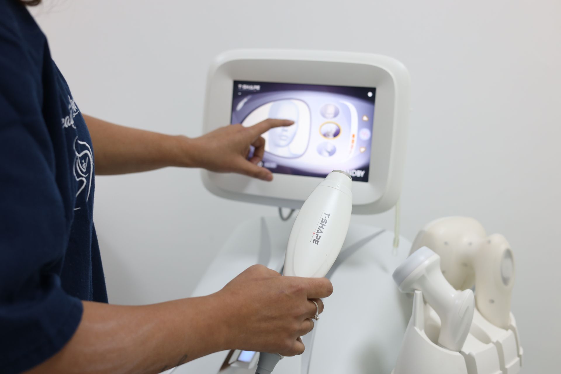 Persona che utilizza un dispositivo medico tramite touchscreen e tiene in mano un applicatore. Sfondo bianco.