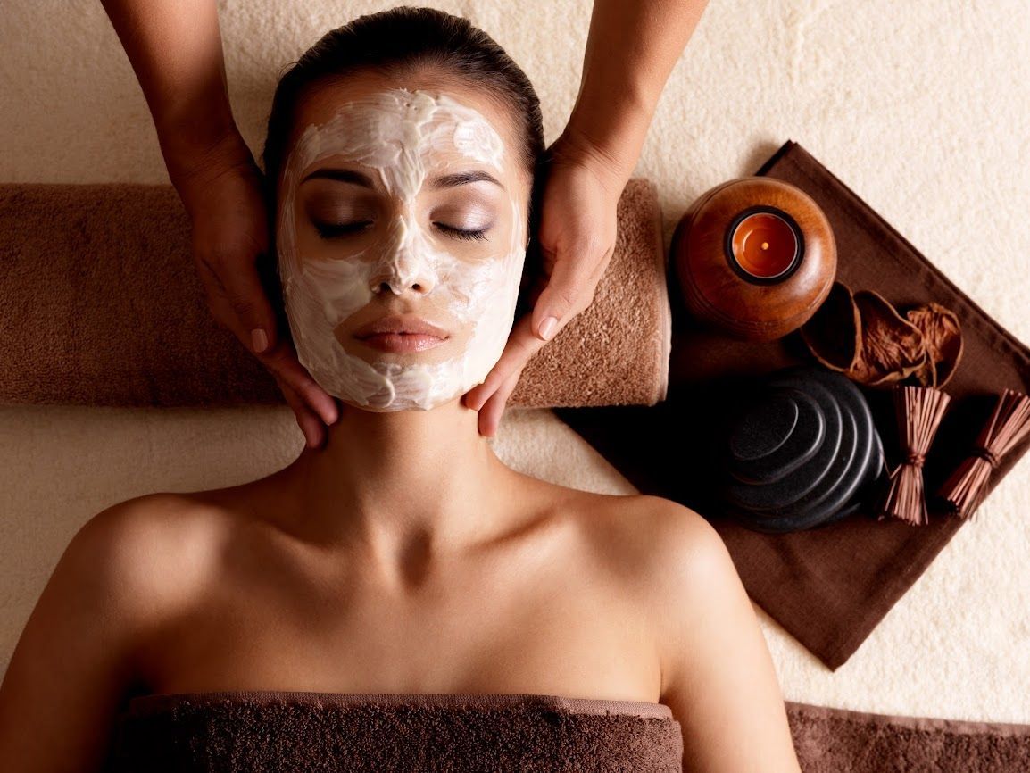 Donna con maschera facciale che riceve un massaggio in una spa; candela e pietre di lato.