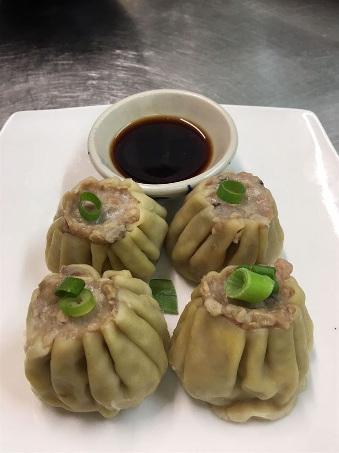 A white plate topped with four dumplings and a bowl of dipping sauce.