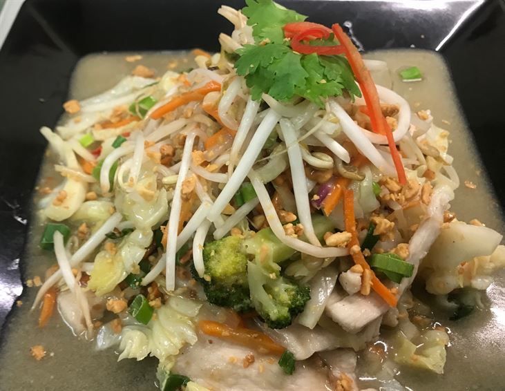 A close up of a plate of food with noodles and vegetables on a table.