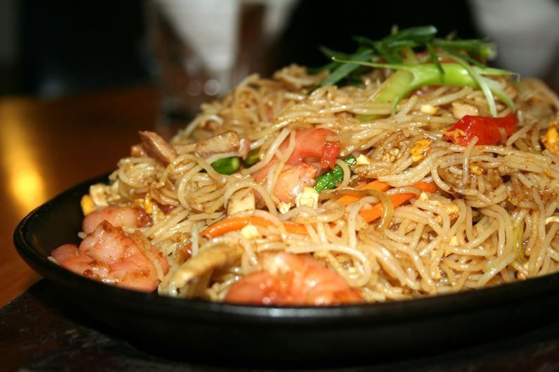 A black bowl filled with noodles and vegetables on a table.