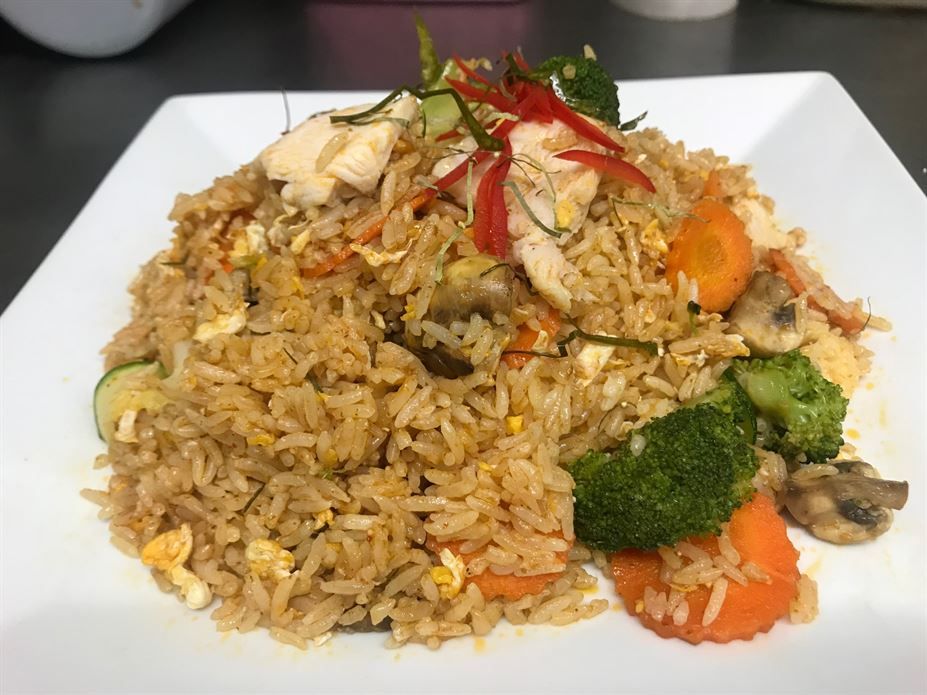 A plate of fried rice with vegetables and chicken on a table.