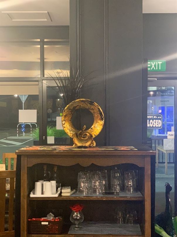 A shelf with glasses and a vase on top of it in a room with an exit sign in the background.