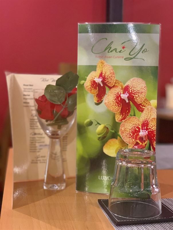 A menu for chai yo sits on a table next to a vase of flowers