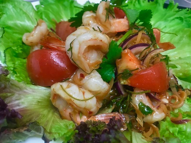 A salad with shrimp , tomatoes , onions and lettuce on a plate.