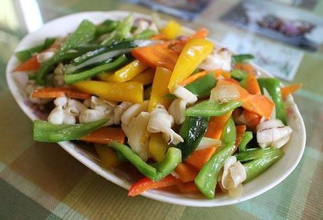 A plate of stir fry vegetables with squid on a table.