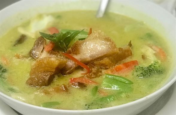 A bowl of green curry with meat and vegetables on a table.