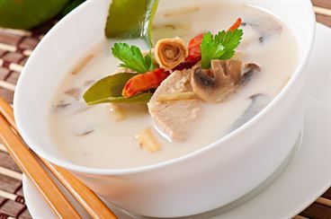 A bowl of soup with vegetables and chopsticks on a plate.