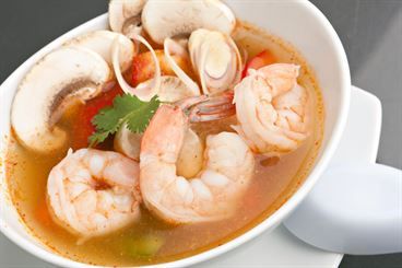 A bowl of soup with shrimp , mushrooms , tomatoes and cilantro.
