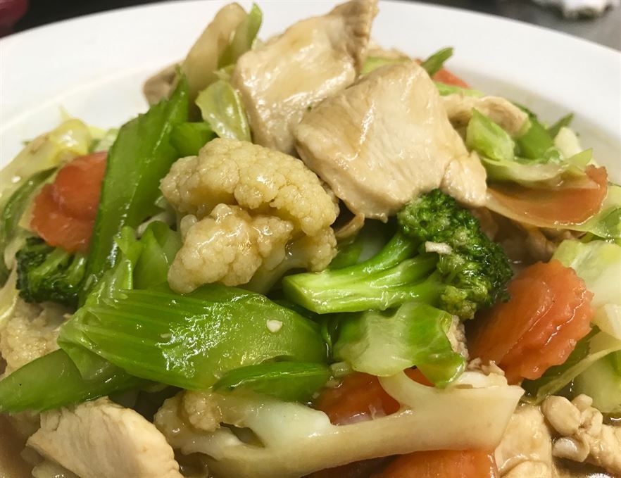 A close up of a plate of food with chicken and vegetables on a table.