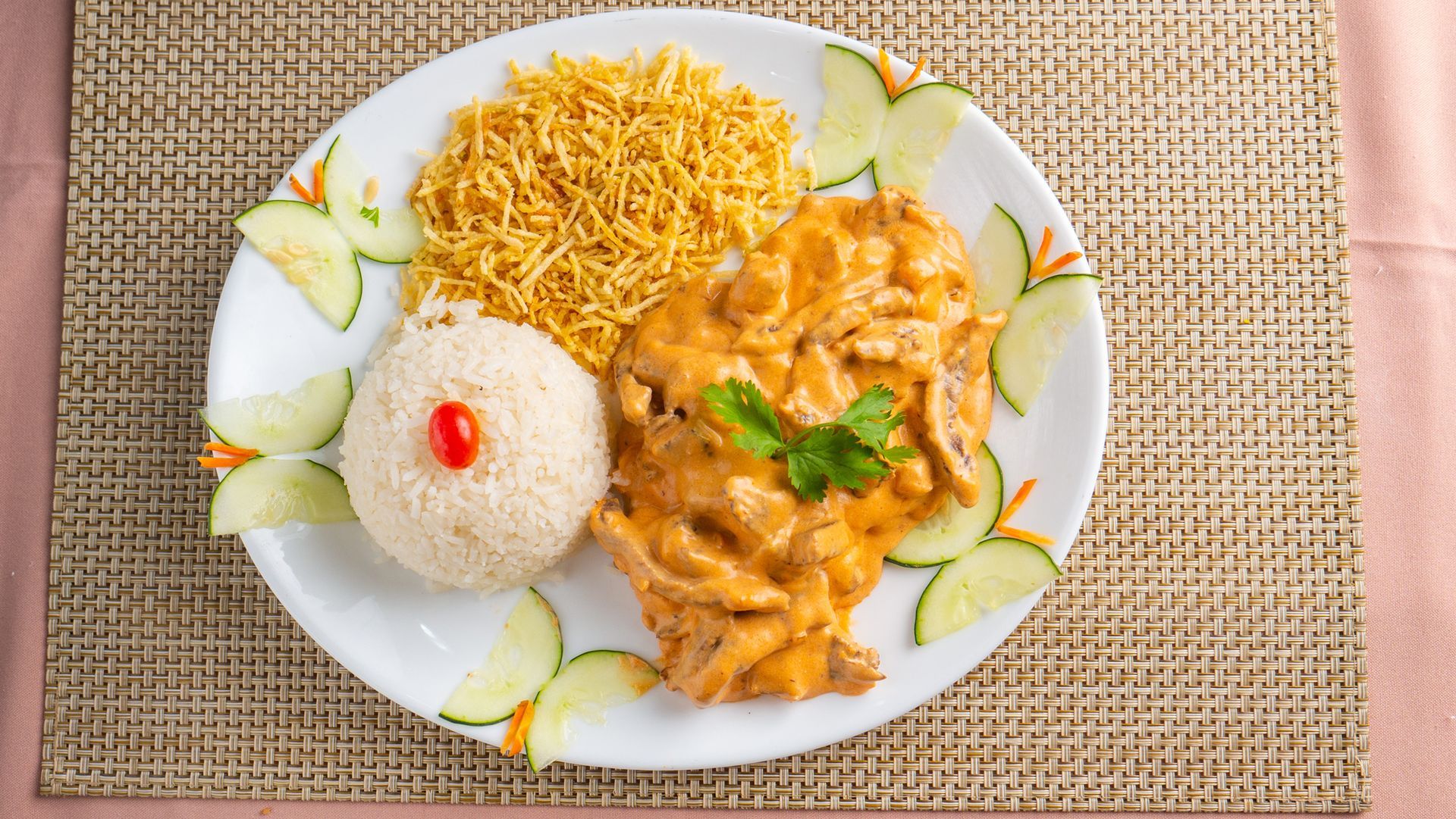 Um prato branco coberto com arroz, frango e pepinos sobre uma mesa.