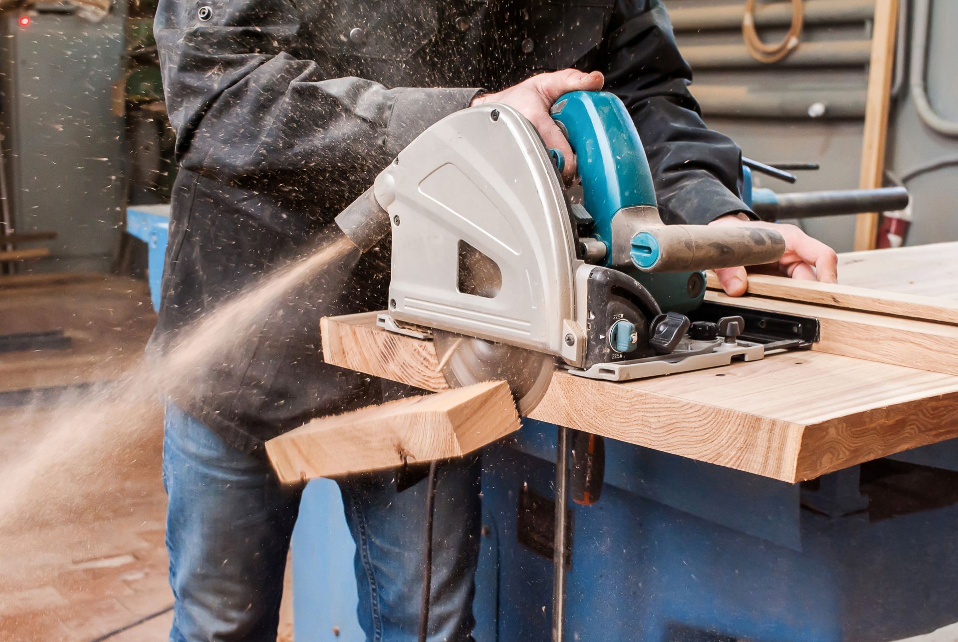 Male carpenter sawing a board with a circular saw in a carpentry workshop close-up.