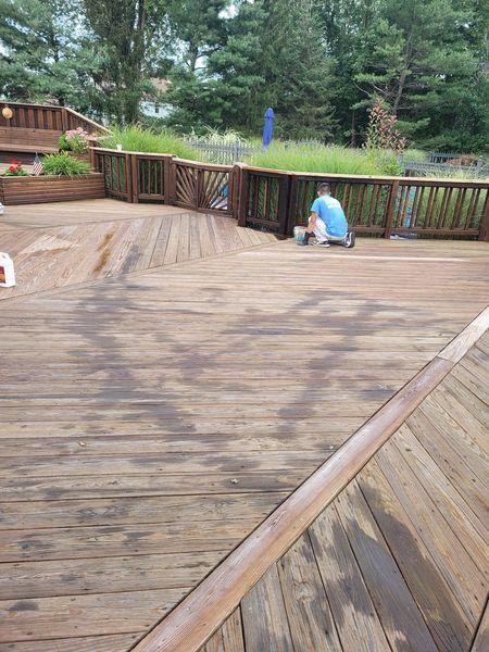 A man is painting a wooden deck with a brush.