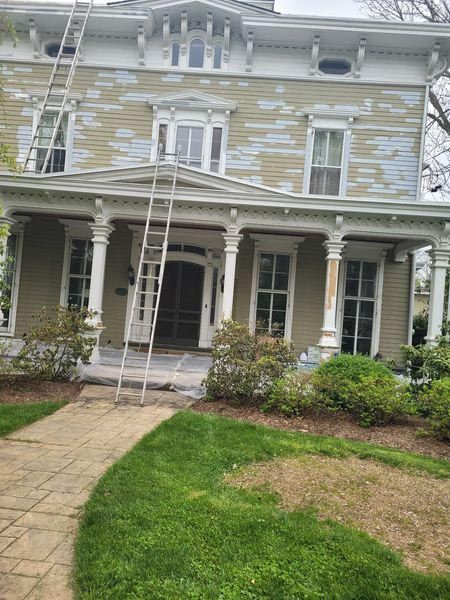 A large house with a ladder on the front of it is being painted.