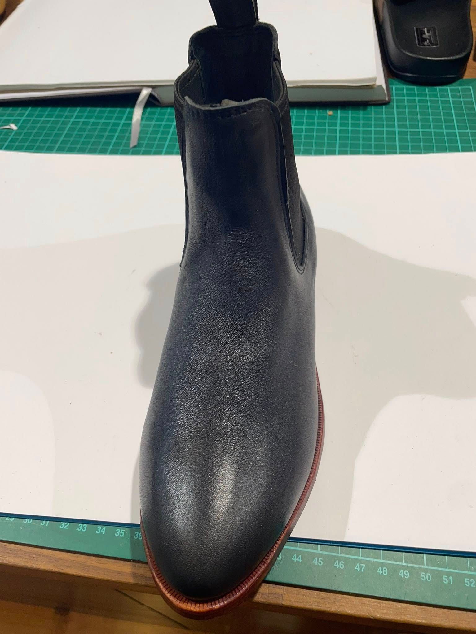 Dark blue leather Chelsea boot with red sole, sitting on a table.