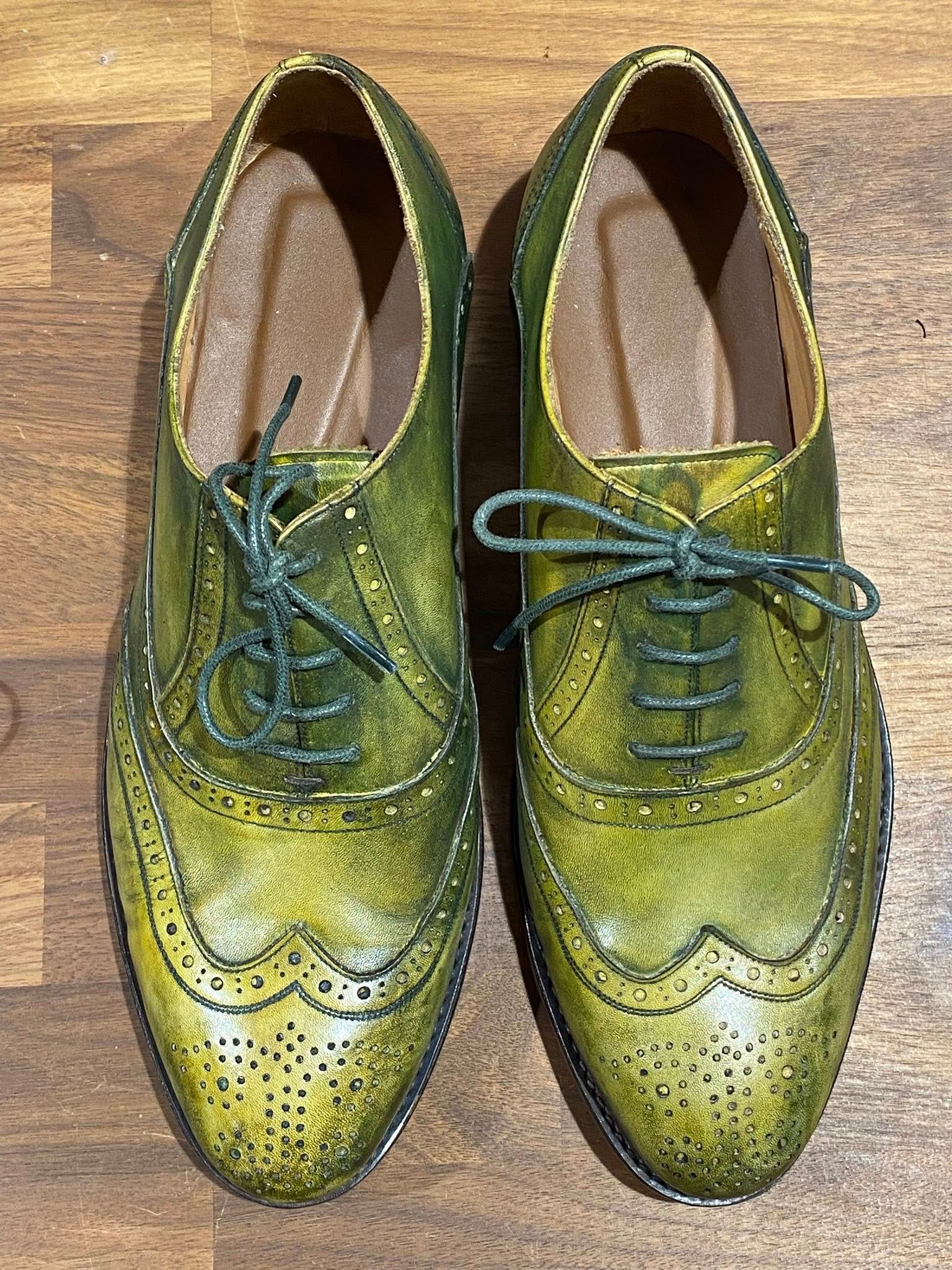 Green leather Oxford shoes with decorative perforations and laces on a wooden surface.