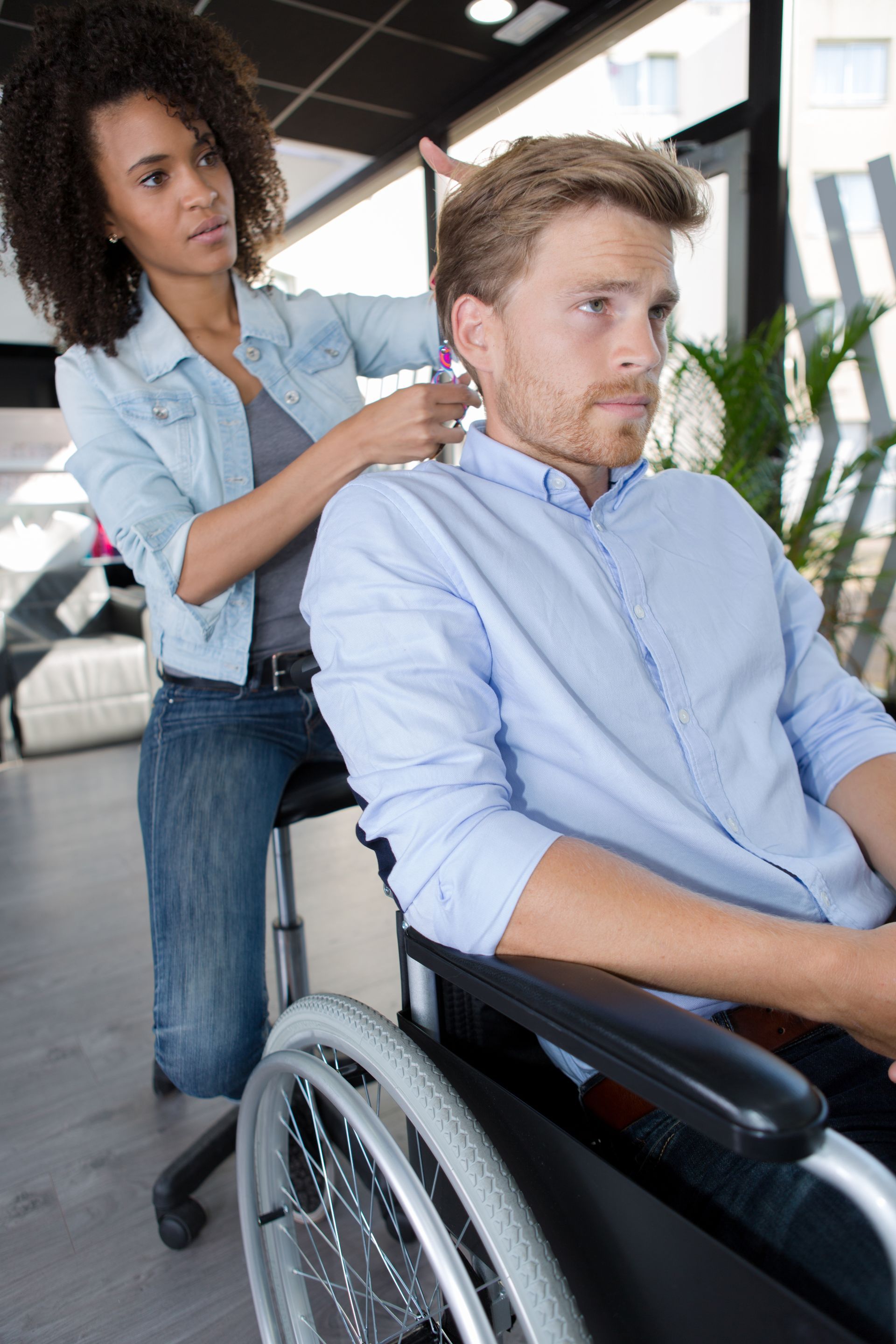 A man in a wheelchair is getting his hair cut by a woman.